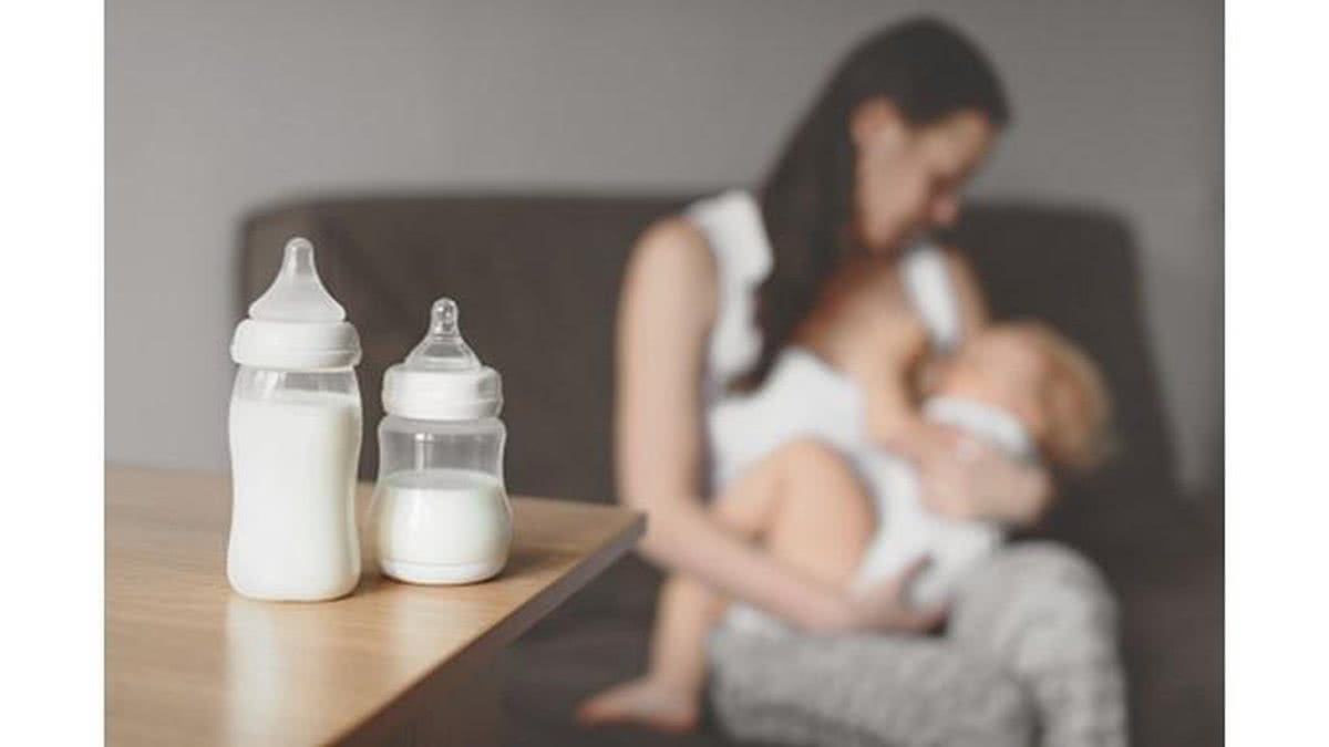 Mãe aparece ao fundo amamentando e na frente mamadeiras com leite - Getty Images
