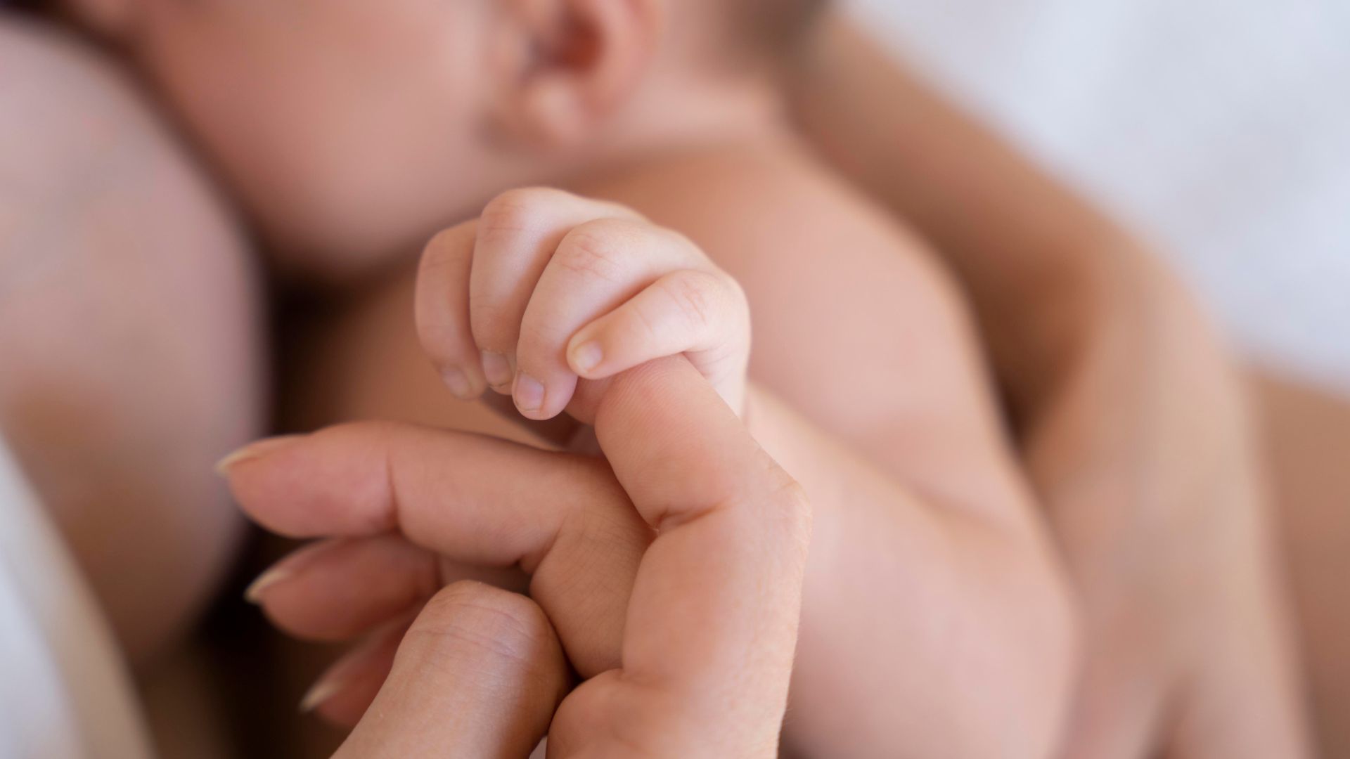Mulher segurando mão de bebê enquanto amamenta