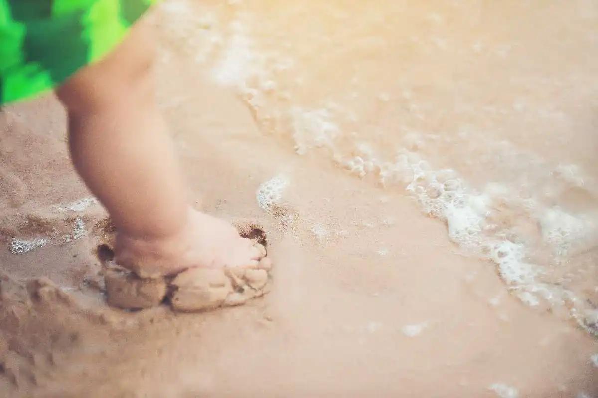 Criança com pé na areia e perto do mar para cuidados com pele atópica