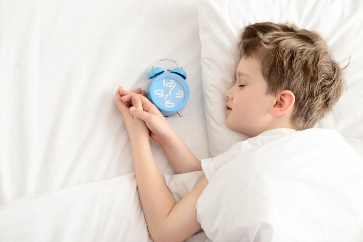 menino dormindo ao lado de um despertador azul