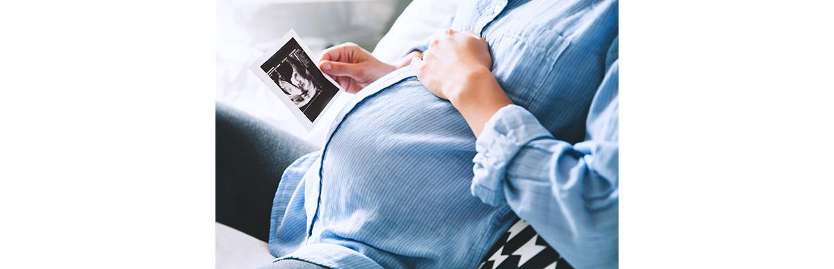 Mulher grávida de camisa com a mão na barriga e olhando ultrassonografia