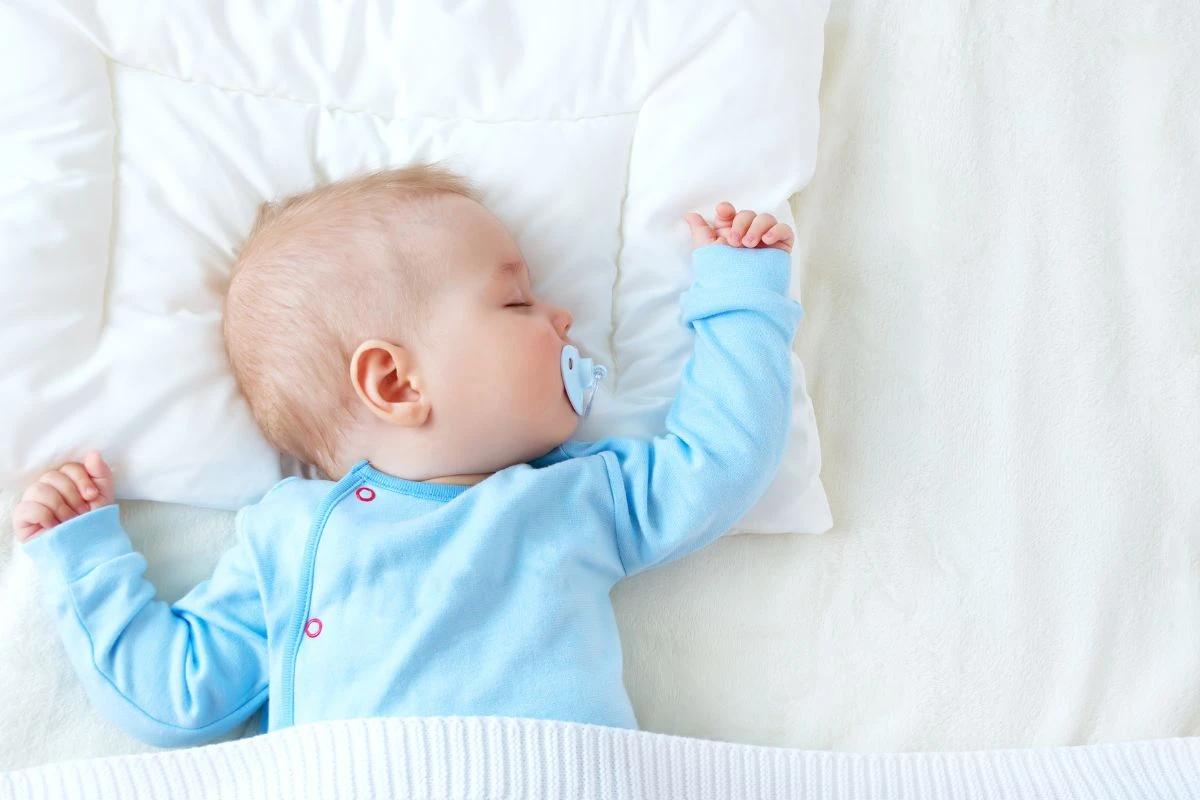 Bebê com chupeta e roupa azul dormindo com a cabeça de lado 