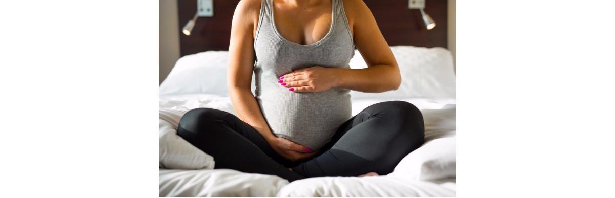 pregnant-woman-sitting-on-bed-with-her-hand-at-belly-picture-id586711028