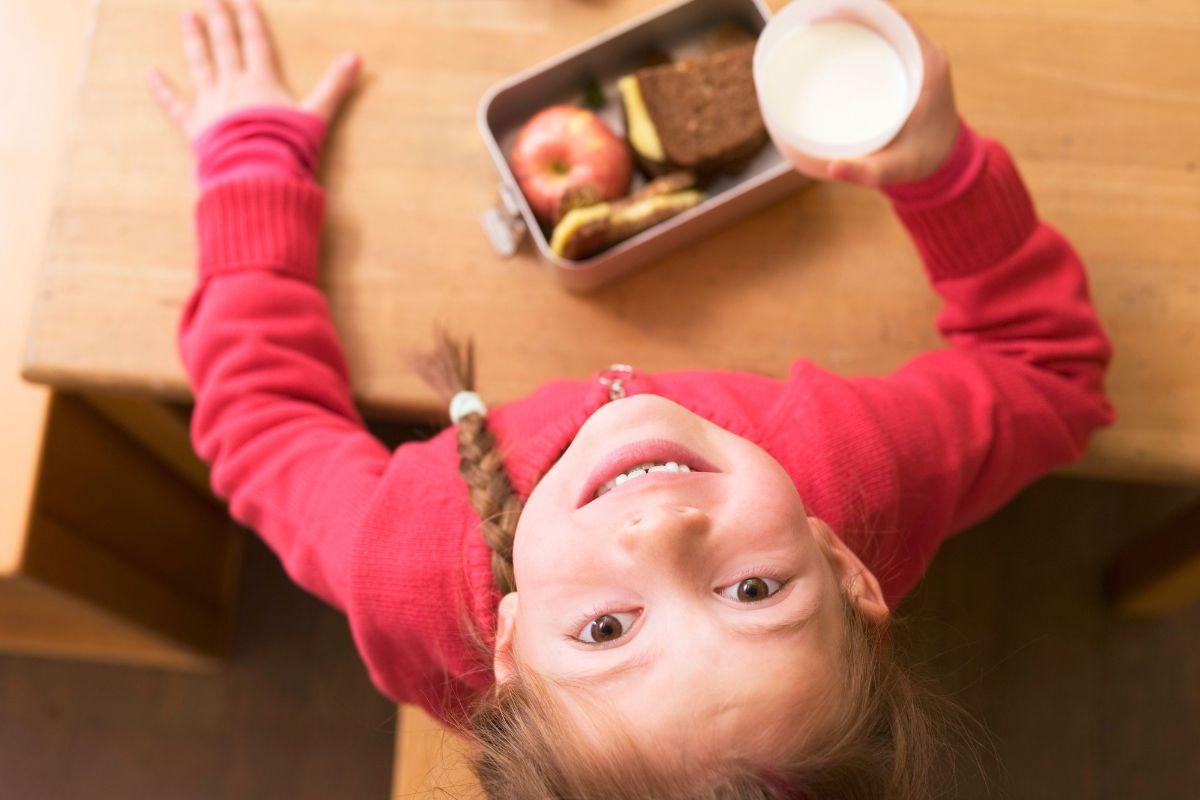 Menina tomando leite com lancheira escolar na mesa 